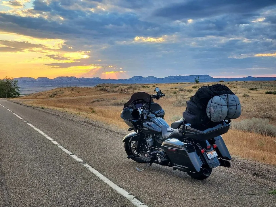 A loaded touring motorcycle beside an open road at sunset